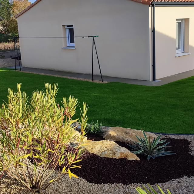 Massif paillé avec rochers et graminées devant une pelouse neuve